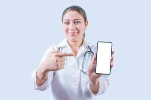 Female doctor showing and pointing an advertisement on the smartphone screen isolated. Smiling female doctor pointing an app on the phone screen photo