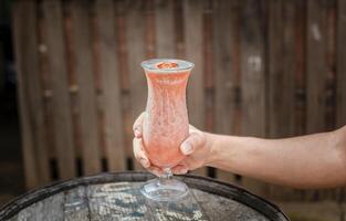 Hands holding strawberry smoothie on wooden table with blurred background. Hands showing strawberry smoothie on wooden table. People hand holding a strawberry milkshake on wood photo