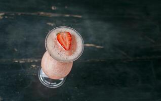 View of strawberry milkshake on dark wood. View from above of delicious strawberry smoothie with a strawberry on top on wood. Top view of strawberry smoothie on dark wooden table photo