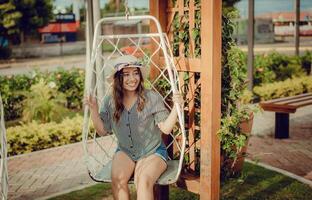 Relaxed girl in hat sitting on a white swing in a beautiful garden. A smiling girl sitting on a swing in La Calzada, Granada, Nicaragua photo