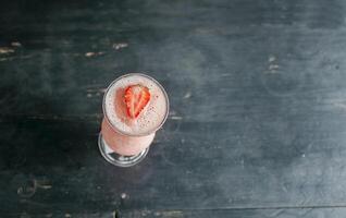 Top view of strawberry smoothie on dark wooden table. View of strawberry milkshake on dark wood. View from above of delicious strawberry smoothie with a strawberry on top on wood photo