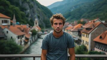 ai generado joven hombre mirando a el cámara mientras en pie en un puente en un antiguo europeo pueblo foto