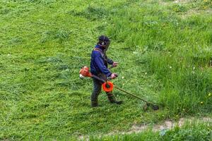 lawnmower man with string trimmer trimming grass at sunny day photo