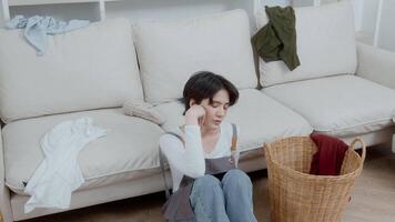 un asiatique Jeune femme gouvernante sentiment fatigué à prendre désordonné sale vêtements dans panier à nettoyer à Accueil video