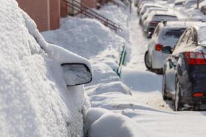 row of snow drifted cars in a row along the street near residential building at winter day snowfall photo