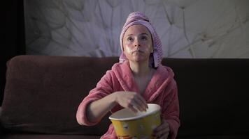 Woman watching a late night movie at TV, eating popcorn. Bathrobe, facial mask video