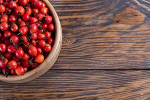 red dog-rose rosehip fruits in a wooden bowl on wooden table photo