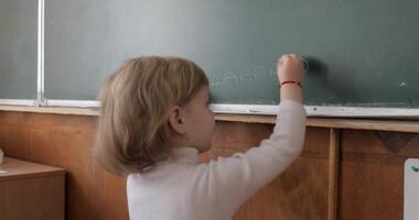 Girl drawing at blackboard using a chalk in classroom. Education process video