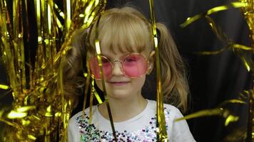 Happy child jumping, playing, fooling around in shiny foil fringe golden curtain. Little blonde girl video