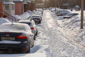 fila de coches a la deriva de nieve en una fila a lo largo de la calle cerca de un edificio residencial en la nevada del día de invierno foto