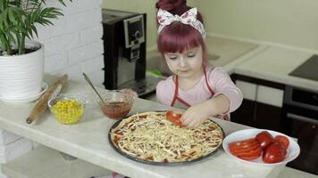 Cocinando Pizza. pequeño niño en delantal agregando rebanado Tomates a masa en cocina video