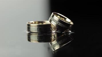 Wedding rings on black and white water surface shining with light. Close up video