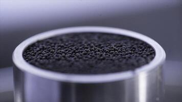 Black grains are checked for quality. Stock footage. Close-up quality control of raw additives with professional equipment in laboratory photo