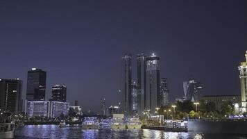 Urban river with ships glowing modern city. Action. Beautiful skyscrapers of modern city glow at night by river. Floating ships on river with city landscape at night photo