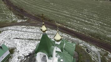 Aerial view of a church with green roof and golden domes. Clip. Church surrounded by green farm fields in early spring. photo