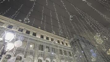 Beautiful hanging garlands on city street. Action. Bottom view of glittering garlands that adorn street. Festive decorations of streets and houses of city shine brightly in evenings photo