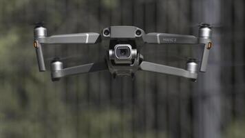 Drone with a camera hovers in the air. Action. Close up of an aircraft and blades that rotate in slow motion on blurred background of green trees, shooting process. photo