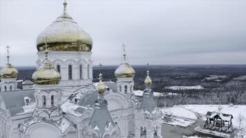 Top view of church on winter cloudy day. Clip. Snowy church with golden domes with forest. Church surrounded by forest in winter photo