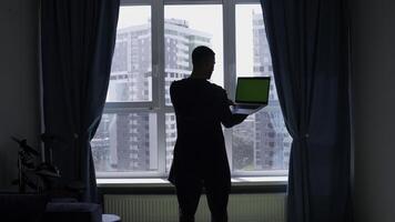 Rear view of a man standing by the window with a laptop in his hands. Media. Computer with green chroma key screen. photo