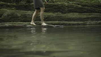 Side view of a man walking barefoot on wet rocks near mountainous water stream. Creative. Forest lake and a man exploring nature. photo