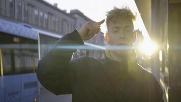 Cheerful young man dancing on street. Action. Young man is dancing merrily at bus stop on sunny day. Man in jacket and headphones dances while waiting for bus photo