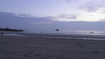 Two people walking on beach with small rocks at sunset. Shot. Beautiful view of the beach, blue sky, and two people walking. photo