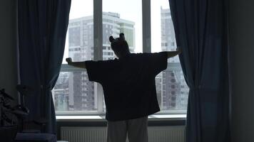 Rear view of a woman stretching while standing by the window. Media. Young girl in a bedroom in the morning. photo