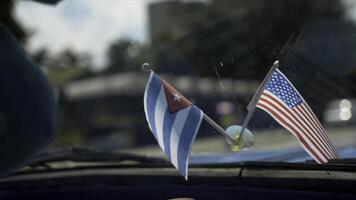 Close-up of flags of America and Cuba in car. Action. Beautiful flags adorn panel of retro car on background of road in hot country. Decoration for car photo