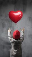 ai generado espalda ver de un niño levantamiento brazos con rojo amor enamorado corazón conformado globo aislado en gris antecedentes foto