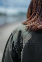 joven hermosa asiático mujer vistiendo chaqueta y negro pantalones posando al aire libre foto