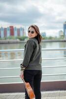 Playing Ukulele of Young Beautiful Asian Woman Wearing Jacket And Black Jeans Posing Outdoors photo