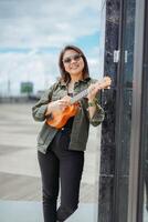 Playing Ukulele of Young Beautiful Asian Woman Wearing Jacket And Black Jeans Posing Outdoors photo