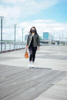 jugando ukelele de joven hermosa asiático mujer vistiendo chaqueta y negro pantalones posando al aire libre foto