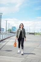 jugando ukelele de joven hermosa asiático mujer vistiendo chaqueta y negro pantalones posando al aire libre foto