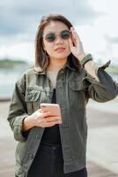 Using Smartphone of Young Beautiful Asian Woman Wearing Jacket And Black Jeans Posing Outdoors photo