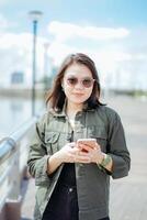 Using Smartphone of Young Beautiful Asian Woman Wearing Jacket And Black Jeans Posing Outdoors photo