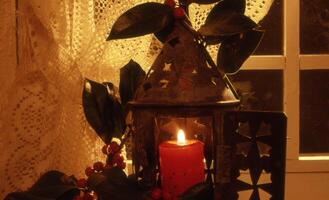 a candle is lit in a lantern with a red holly leaf photo