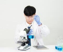 retrato asiático hombre estudiante científico vistiendo un médico vestido en el laboratorio mirando mano a químico. causado por mezcla reactivos en científico investigación laboratorios con prueba tubos y microscopio en el mesa foto