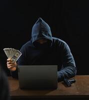 Portrait hacker spy man one person in black hoodie sitting on table looking computer laptop used login password attack security to data digital internet network system night dark background copy space photo