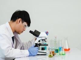 retrato asiático hombre estudiante científico vistiendo un médico vestido en el laboratorio mirando mano a químico. causado por mezcla reactivos en científico investigación laboratorios con prueba tubos y microscopio en el mesa foto