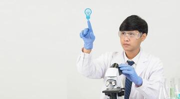 retrato asiático hombre estudiante científico vistiendo un médico vestido en el laboratorio mirando mano a químico. causado por mezcla reactivos en científico investigación laboratorios con prueba tubos y microscopio en el mesa foto