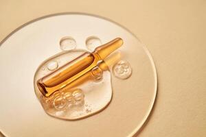 Ampoule in a drop of cosmetic gel on a beige background. photo