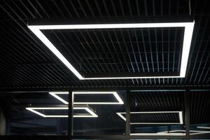iluminación de oficina moderna. lámparas delgadas en el techo oscuro de la oficina. led de luz blanca fria sobre lugares de trabajo. foto