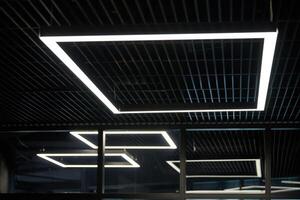 Modern office lighting. Thin lamps in office dark ceiling. LED white cold light over workplaces. photo