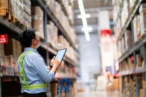 Warehouse worker in security uniform with tablet computer looking at merchandise in large warehouse Logistics and export business Logistics distribution center. photo