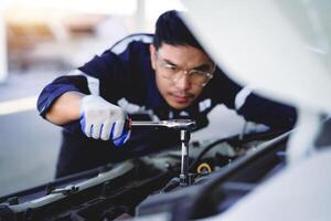 auto mecánico es trabajando en coche motor en mecánico tienda. un mecánico en uniforme es trabajando en un coche servicio. trabajo en reparar tiendas y mantenimiento servicios. foto