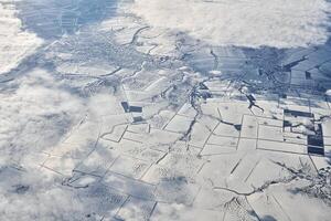Aerial view over clouds top to snow covered rivers, fields and roads, winter fresh frosty air photo
