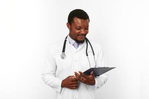 Smiling black bearded doctor man in white robe with stethoscope looks to medical chart on clipboard photo