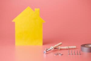 concepto de renovación de la casa. reparar y redecorar el hogar. tornillos y figura en forma de casa amarilla sobre fondo rosa. foto