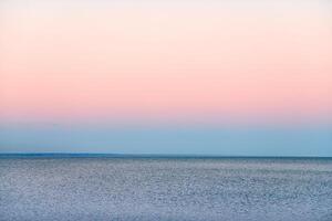 Atmospheric romantic pink red sea sunset sky above blue quiet water, minimalistic peaceful seascape photo